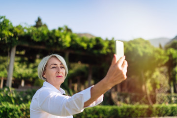 Happy mature woman taking a selfie with mobile phone while resting at the park 