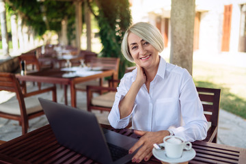 Confident senior woman sitting at a cafe with laptop computer and drinking coffee