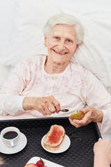 Glückliche Seniorin beim Frühstück im Bett