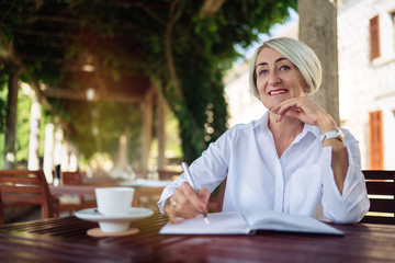 Happy senior woman writing to notebook or diary at a cafe