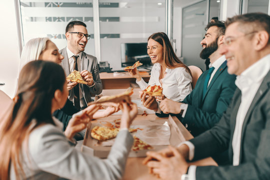 Small group of happy colleagues in formal wear chatting and eating pizza together for lunch. Alone we can do so little, together we can do so much. - Powered by Adobe