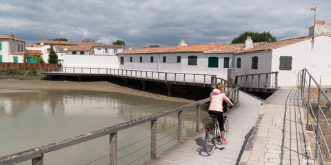 Young woman riding with bicycle on a wooden path to beach in Summer sunny day on island ile de Re...