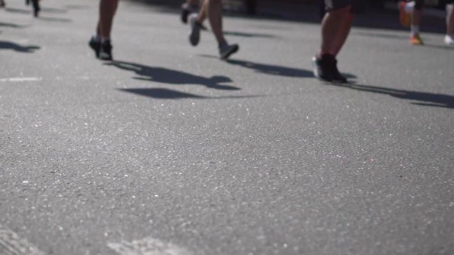 Participants of the marathon run along the road on a city street on a sunny spring day. Slow motion. Legs close-up. Sport and healthy lifestyle. Run at the marathon