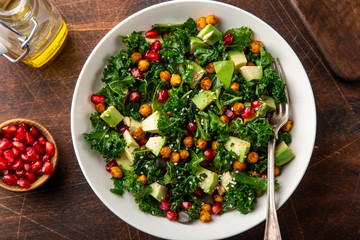 avocado, kale, roasted chickpeas, almond and pomegranate salad in white bowl