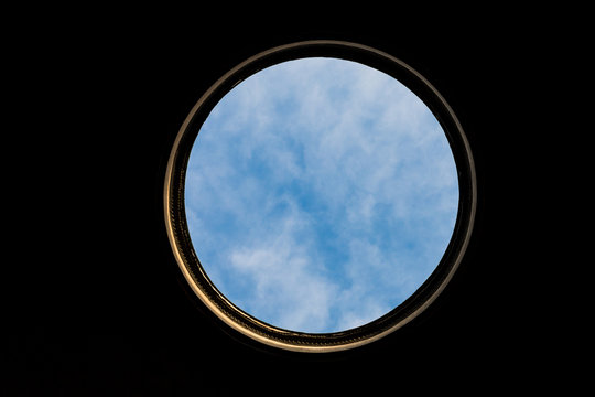 Large circular hole with golden frame and blue cloudy sky and black background.