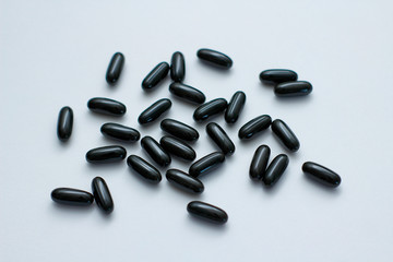 Many black oval pills on white background. Capsules with liquid. Supplements. 
