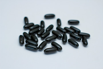 Many black oval pills on white background. Capsules with liquid. Supplements. 