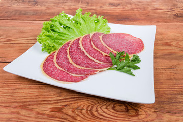 Slices of parmesan coated salami, greens on square dish