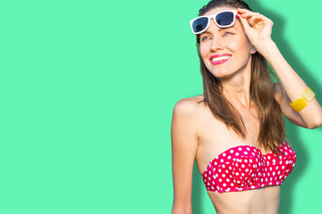 Portrait of a young girl in fashionable swimsuit and sunglasses over bright geen blue background