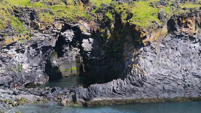 Closeup landscape view of hiking trail of rocky beach Valasnos rock cliff in Hellnar national park in Snaefellsnes Peninsula, Iceland with ocean sea waves, green grass in summer with people