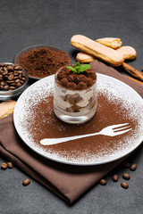 Classic tiramisu dessert in a glass and cup of coffee on dark concrete background