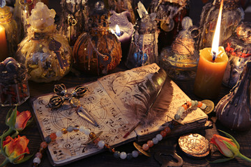 Witch book with cross, quill, burning candles and magic bottles on the table.