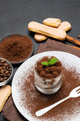 Classic tiramisu dessert in a glass and cup of coffee on dark concrete background