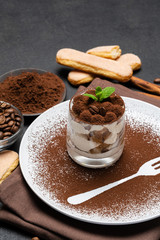 Classic tiramisu dessert in a glass and cup of coffee on dark concrete background
