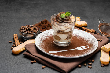 Classic tiramisu dessert in a glass and cup of coffee on dark concrete background
