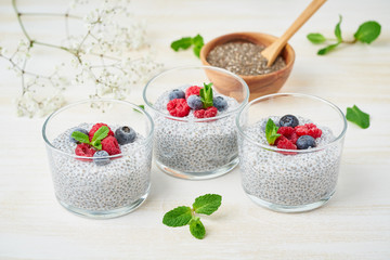 Chia pudding with fresh berries raspberries, blueberries. Three glass, light wooden background, side view, flowers.