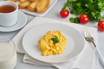 Scrambled eggs, omelette, side view. Breakfast with pan-fried eggs, glass of milk, tomatoes on white background.