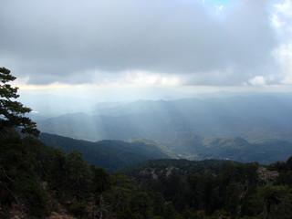 An unusual natural picture of the rays of the sun that penetrates through a heavy gray cloud to dense forests on the slopes of the mountains.