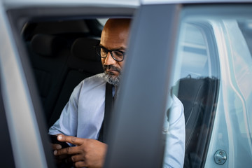 Mature african businessman using smartphone in car