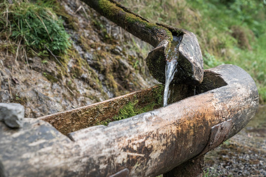 Mountain natural water spring out of wooden gutter from rocky creek at the Vertova torrent near Bergamo.
