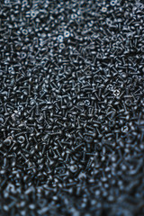 Many black small screws for repair and fasteners in a box close-up.