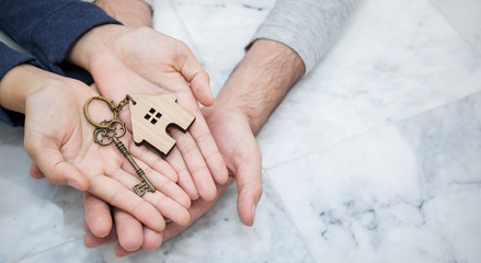 Closeup real estate or couple hands holding and giving key house with copy space isolated on marble...