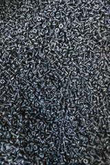 Many black small screws for repair and fasteners in a box close-up.
