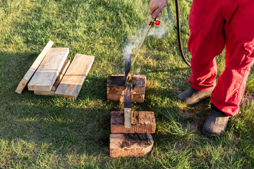 A man burns wooden planks with propane using old-time Japanese technology, creating facing material for building a house