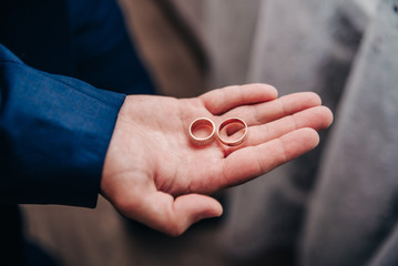 groom holds gold wedding rings in his palm