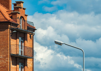 Fototapeta premium Street lamp against a cloudy sky next to a vintage brick building