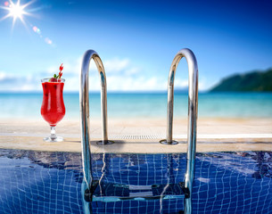 Fresh cold summer drink of red color. swimming pool background with sea and beach landscape. Summer sunny day. 