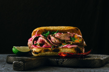 Grilled spicy steak sandwiches on wooden cutting boards on dark background
