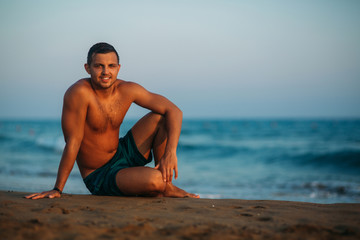 Fototapeta na wymiar Handsome man on a sandy beach sits on the seashore. Young man on the coast