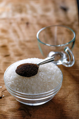 Sugar with tea spoon in glass bowl on wooden background