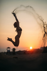 Sexy girl jumps up and throws sand. Silhouette of woman in the air