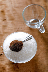 Sugar with tea spoon in glass bowl on wooden background