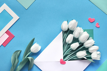 Springtime flat lay, white tulips in paper envelope on blue mint background with envelopes, cards and decorative hearts