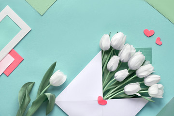 White tulips in paper envelope on blue mint background with envelopes, cards and decorative hearts