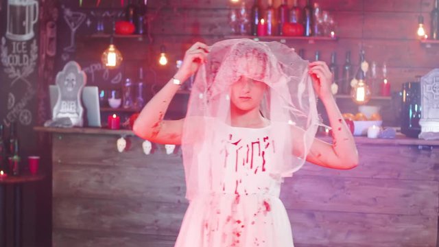 Teenage girl dressed in a dead bride costume before a halloween party. Young girl playing dead with a brides dress painted in blood.