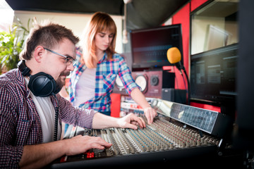 Music producer and musician in recording studio using soundboard for mixing sound