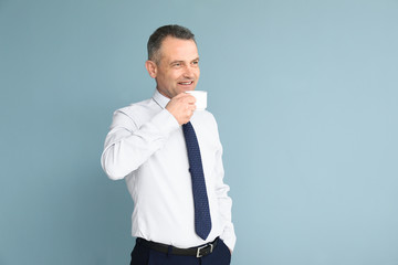 Handsome mature businessman drinking coffee on color background