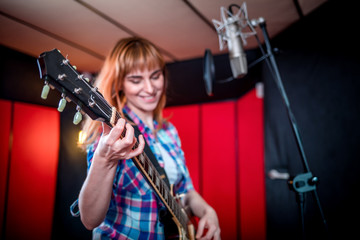 Female singer with electric guitar recording a song in studio