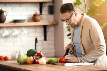 Handsome mature man preparing salad in kitchen