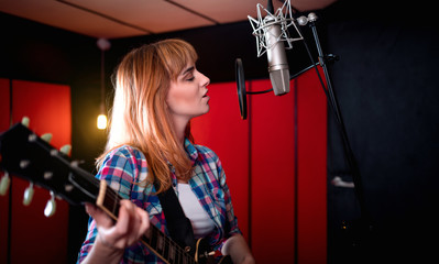 Fototapeta na wymiar Female singer with electric guitar recording a song in studio