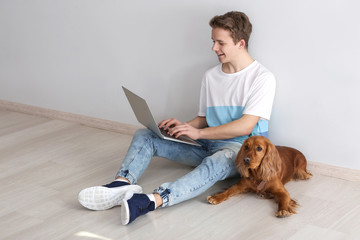 Teenage boy with cute dog and laptop sitting near light wall