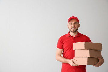 Handsome delivery man with boxes on light background