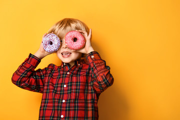 Happy little boy with tasty donuts on color background