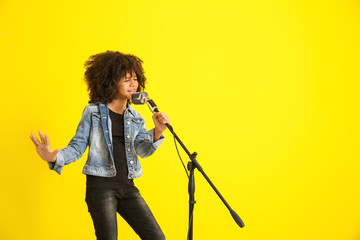 African-American girl with microphone singing against color background