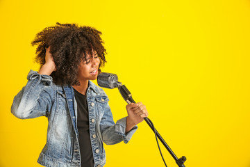 African-American girl with microphone singing against color background