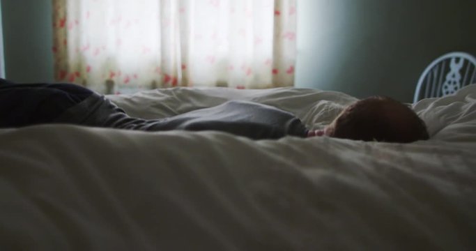 4K Exhausted man falling face down onto his bed in the early hours of the morning. Slow motion.
